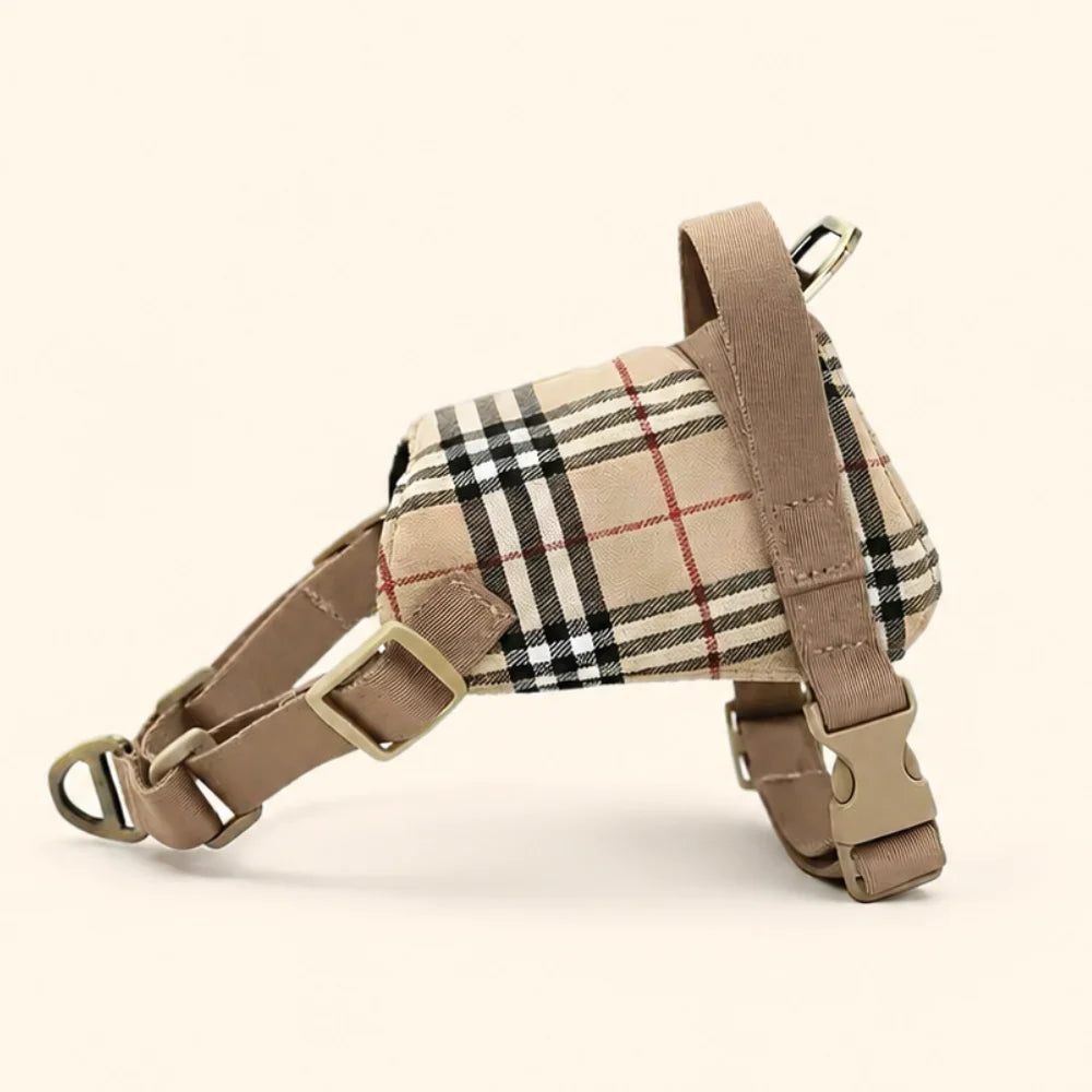 A small dog harness in beige tartan plaid fabric with tan leather straps and gold-tone metal hardware, photographed on a clean cream background.
